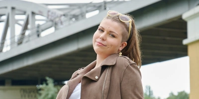 Auszubildende Michelle sitzt im Park vor einem U-Bahnaquädukt