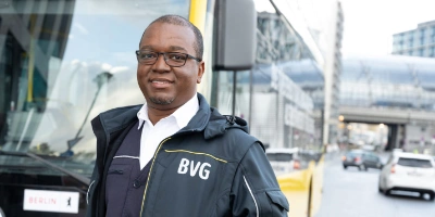 Busfahrer Salem steht in BVG-FAhrdienstkleidung vor einem Bus