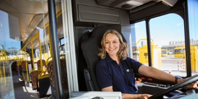 BVG-Busfahrerin sitzt im Bus am Steuer und lächelt richtung Eingangsbereich.