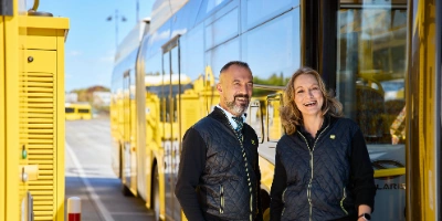 Busfahrerin und Busfahrer stehen vor einem E-Bus auf dem Betriebshof