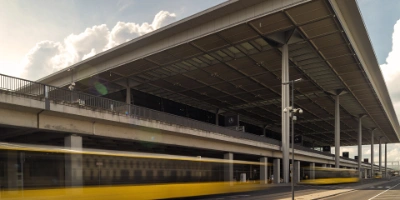 Sicht auf den BER, eine Tram fährt ein. Im Hintergrund entsteht eine spannende Lichtstimmung durch Wolken und Sonne.