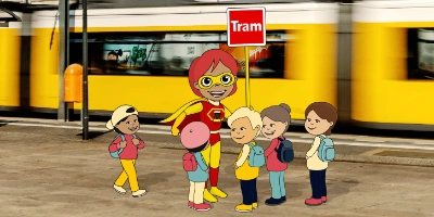 Im Vordergrund ist Tamara und eine Gruppe von Kindern. Im Hintergrund ist eine Tram.
