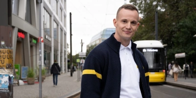 Straßenbahnfahrer Nico steht auf einer Verkehrsinsel in Berlin Mitte - im Hintergrund fährt eine Straßenbahn