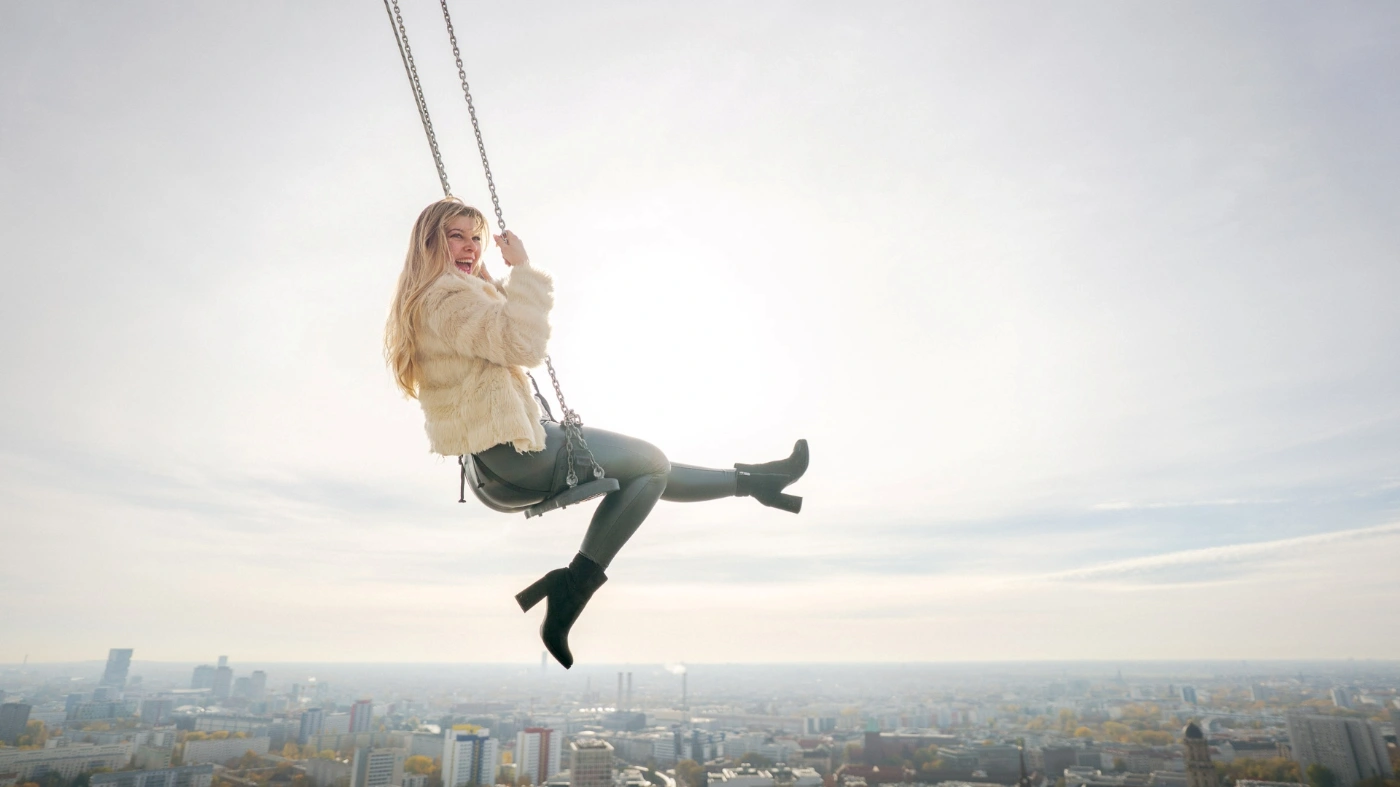 Eine Person schaukelt in hoher Höhe mit der Aussicht auf Berlin.