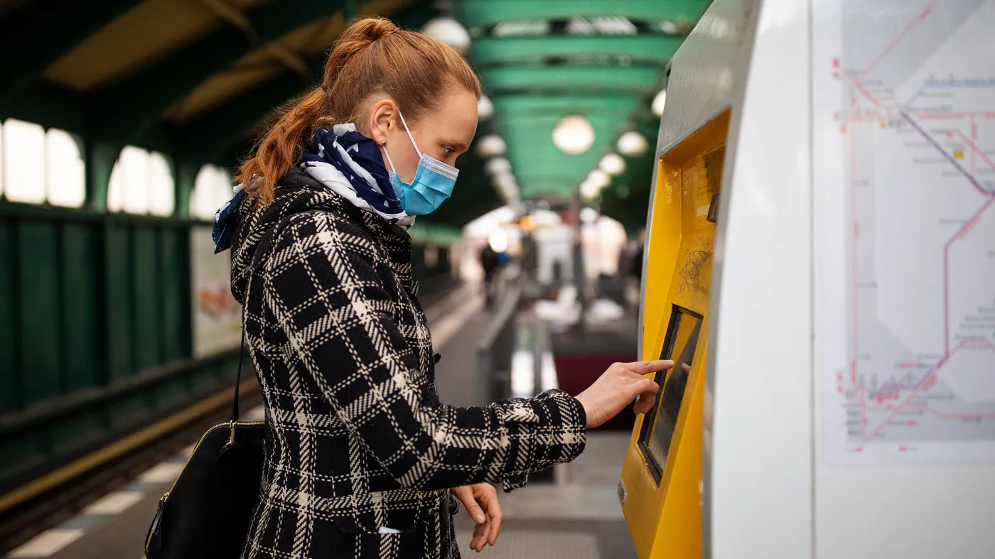 A woman in a mask is operating a ticket machine.