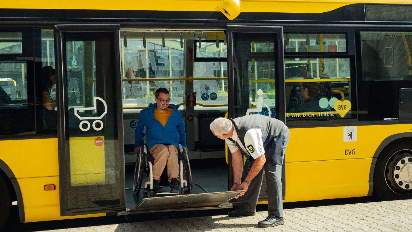 A wheelchair user waits for a BVG employee to attach a ramp to the bus door.