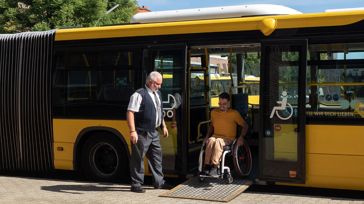 A man in a wheelchair leaves a bus via a ramp.