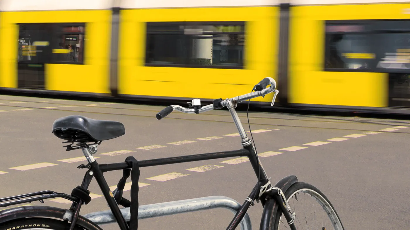 Ein schwarzes Fahrrad steht angeschlossen an einer Straße. Im Hintergrund fährt eine Tram.