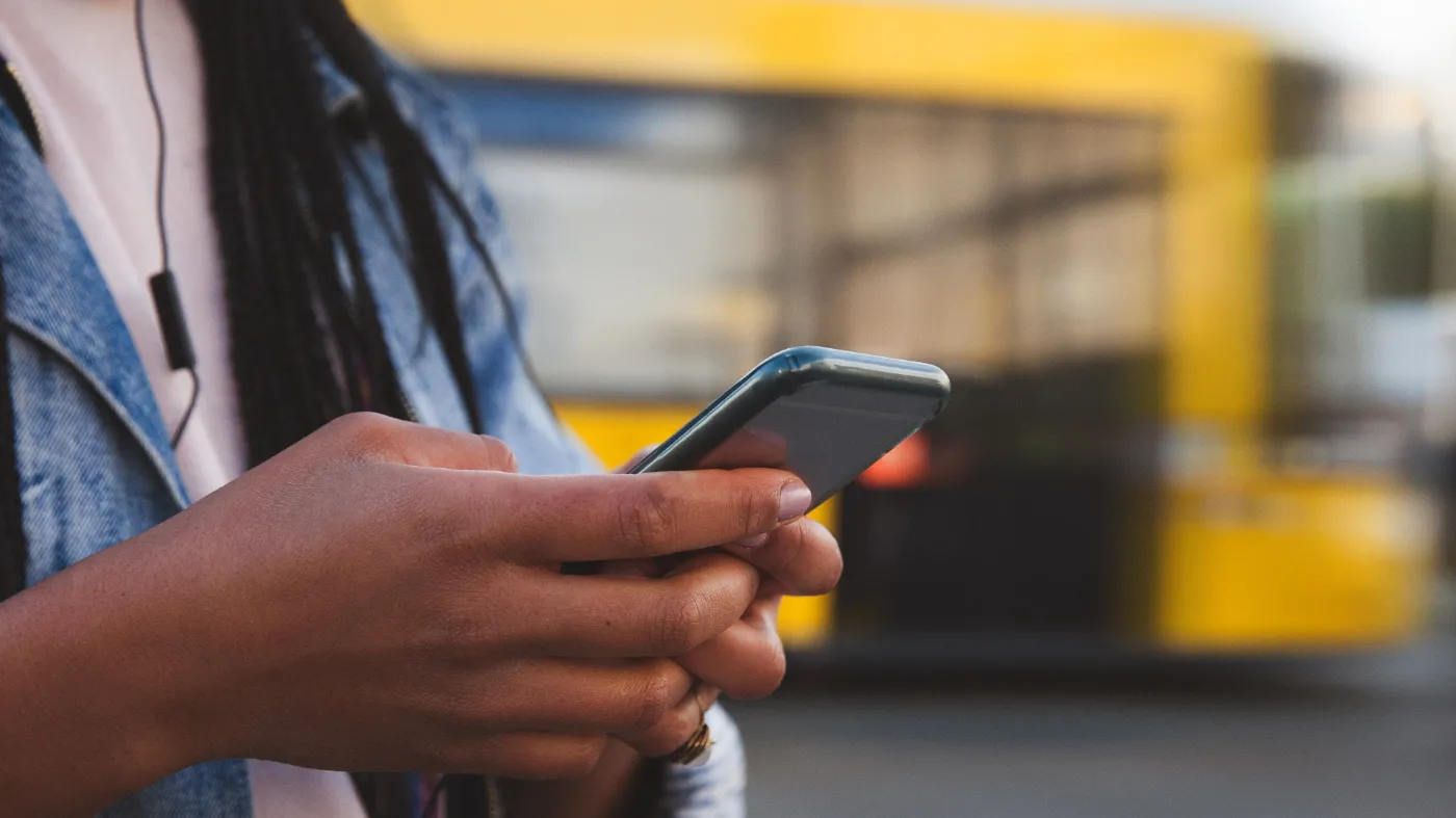 A person is operating a smartphone. A BVG bus can be seen blurred in the background.