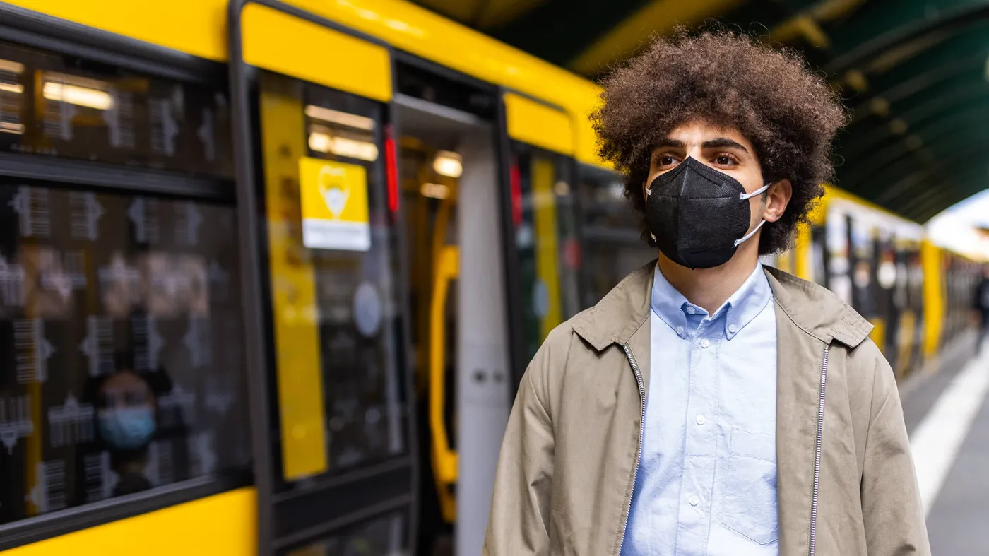 Eine männlich gelesene Person verlässt noch immer eine schwarze FFP2-Maske tragend die U-Bahn. 