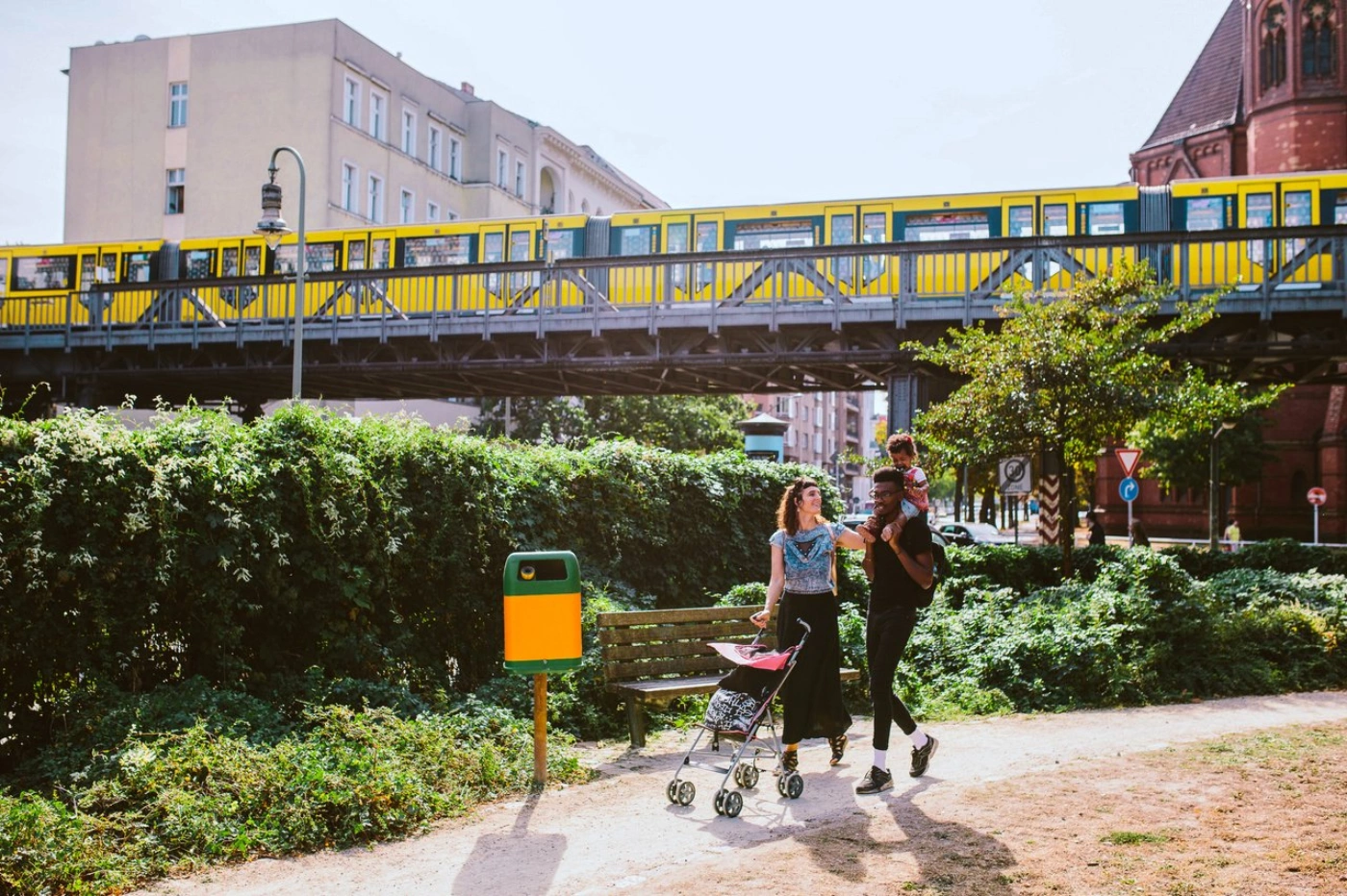 En junges Paar picknickt auf einer Wiese. Im Hintergrund fährt ein Bus der BVG vorbei. 