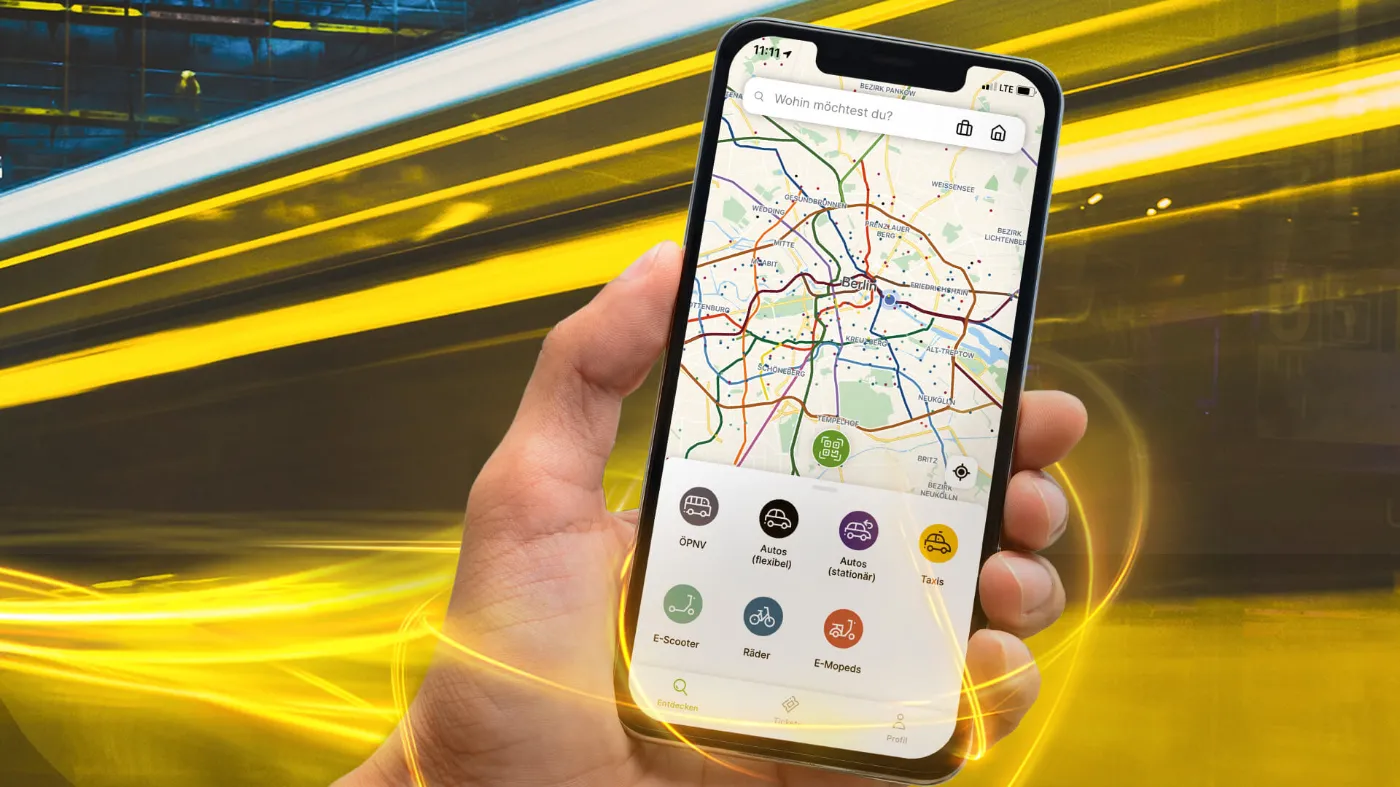 Eine Hand hält ein Smartphone, auf dem Bildschirm ist der Homescreen der Jelbi-App zu sehen. Eine Berlinkarte und die Buchungsoptionen in Form von farbigen Icons werden gezeigt,
