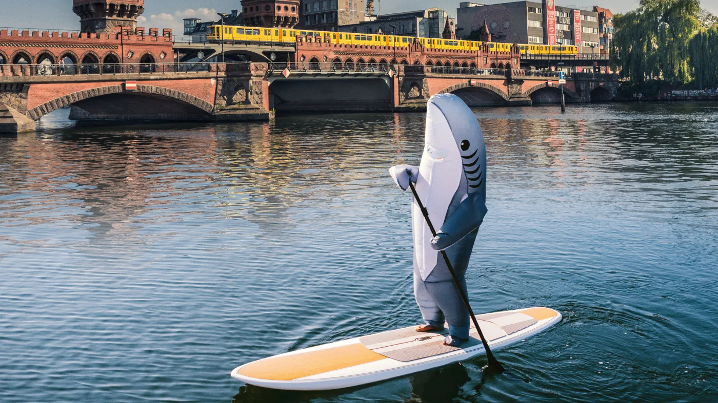 Als Hai verkleidete Person auf einem SUP vor der Warschauer Brücke