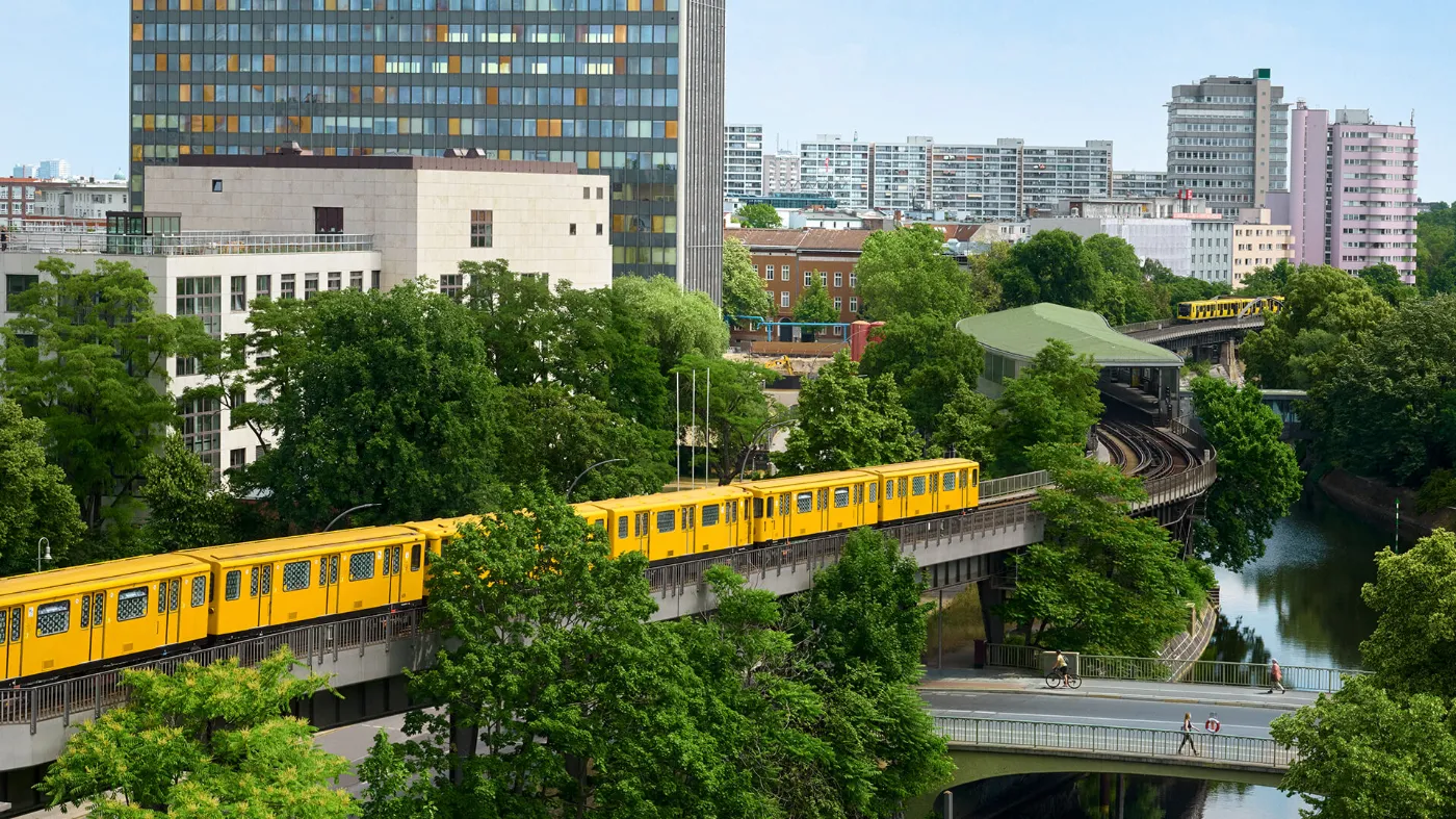Eine U-Bahn fährt entlang der Spree neben Wohn- und Bürogebäuden.