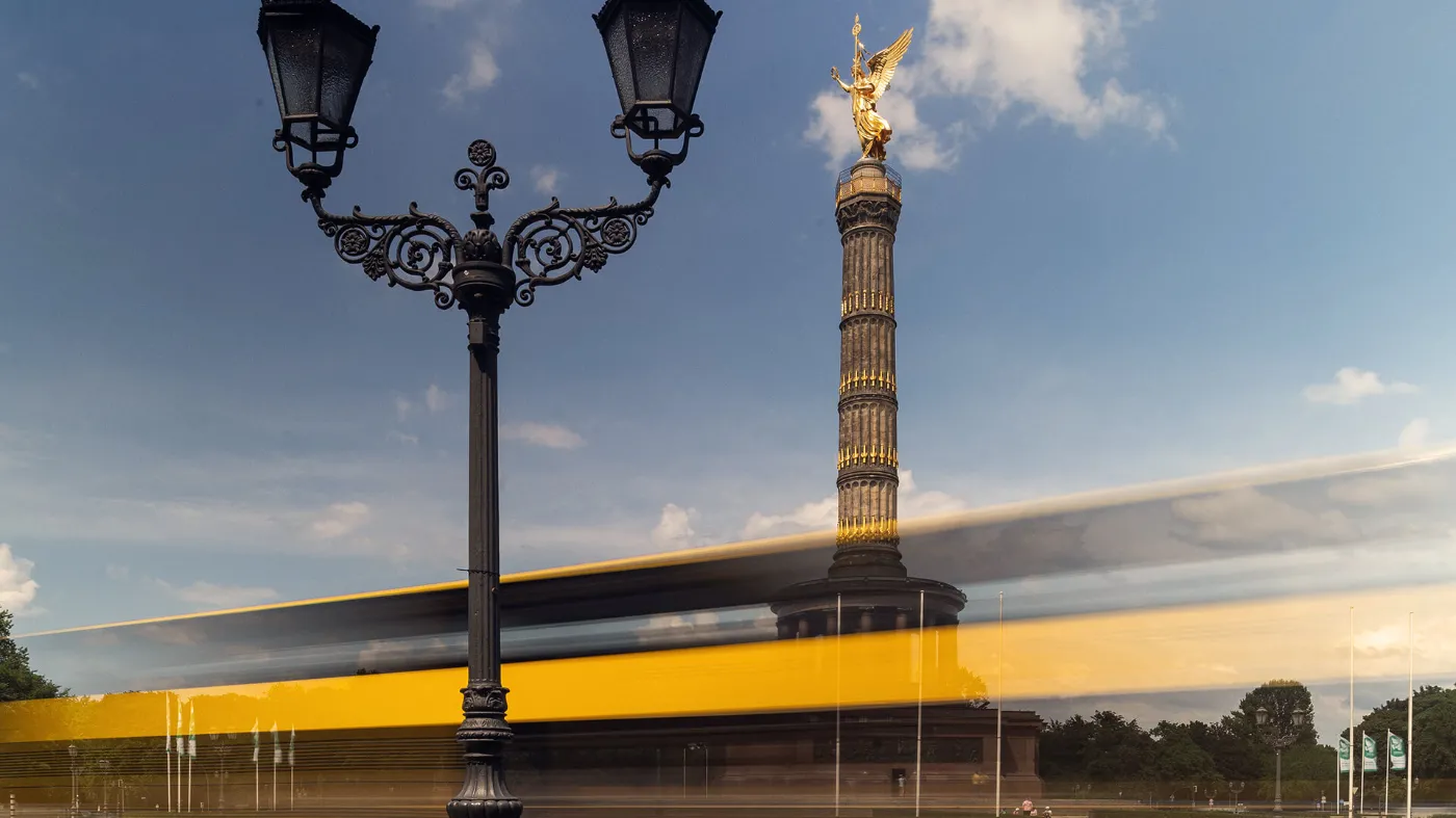 Blick auf die "Goldelse", vor der ein Bus der BVG fährt. Im Vordergrund steht eine antike Laterne. 
