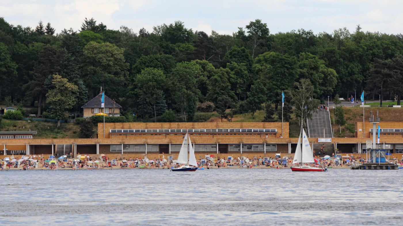 Zu sehen ist der Blick auf das Freibad am Wannsee. Am Strand sind viele Menschen und Strandkörbe.