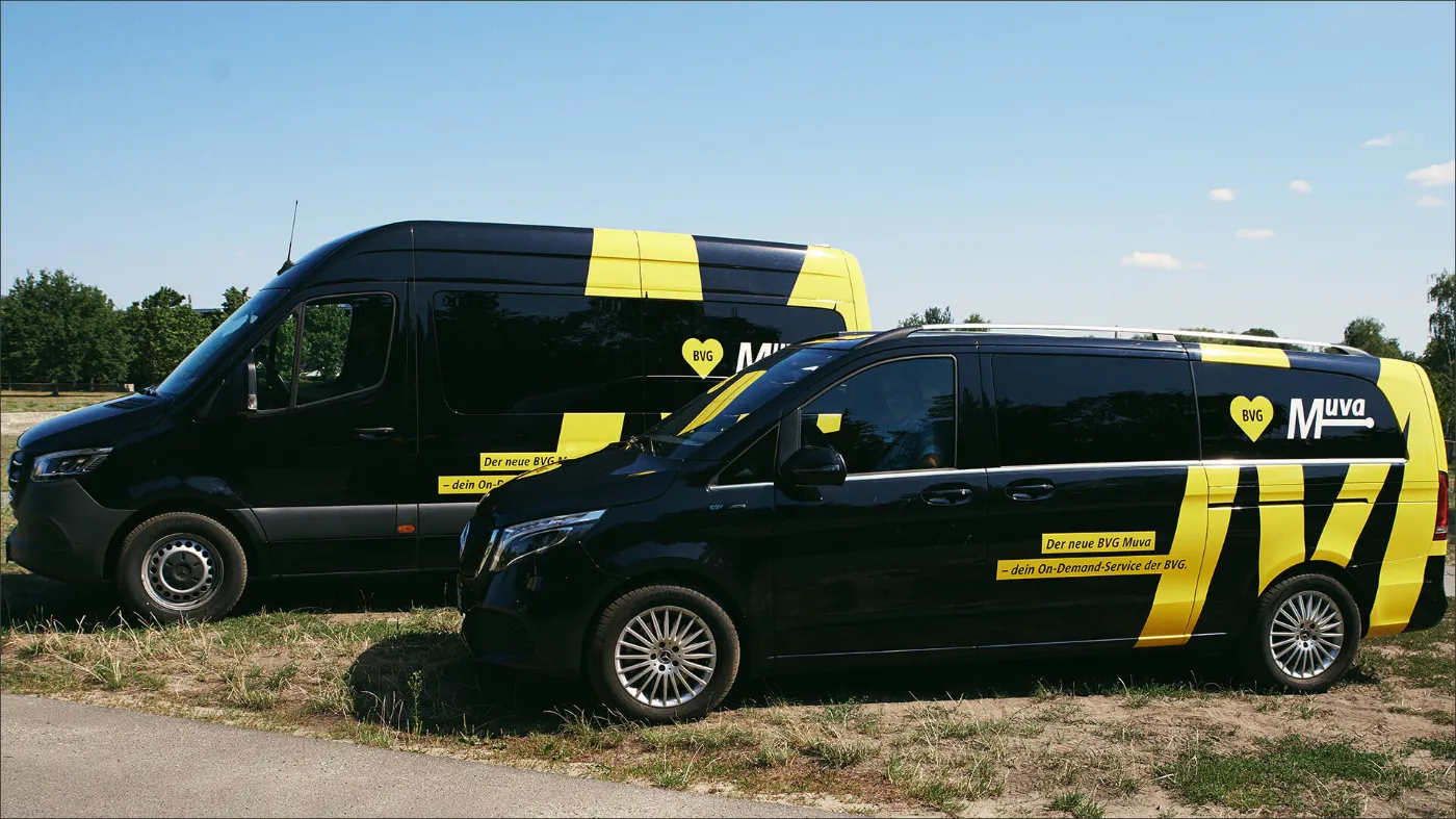 Zwei Fahrzeuge des BVG Muva stehen auf einer Wiese. Es handelt sich um schwarze Transporter mit gelbem BVG Muva-Aufdruck. 