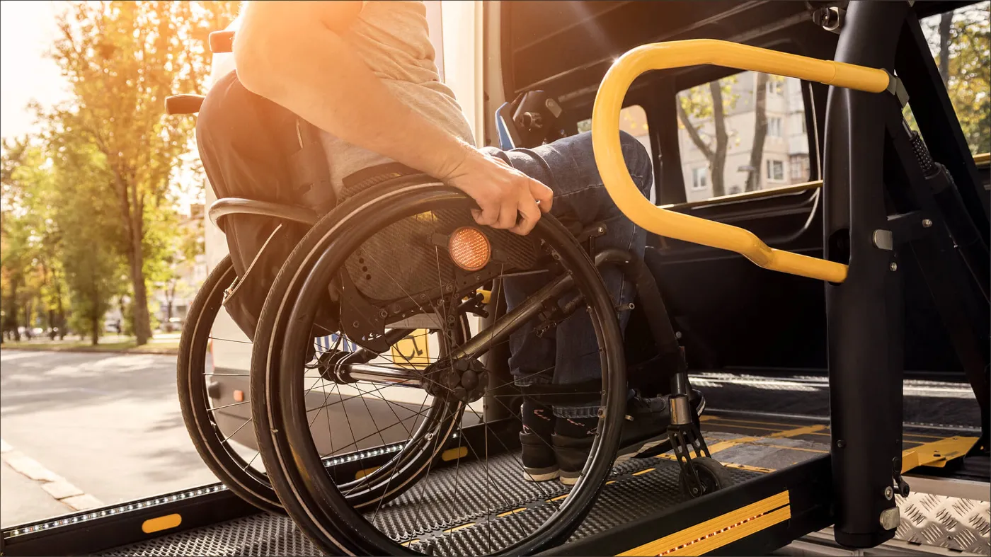 Nahaufnahme einer Person im Rollstohl, die gerade über eine Rampe in einen Bus der BVG fährt. 