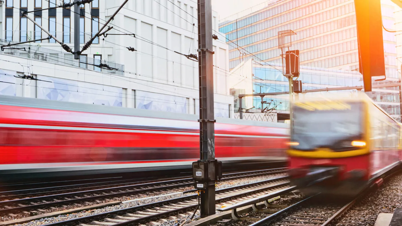 Eine Regionalbahn und eine S-Bahn fahren auf Schienen in entgegengesetzte Richtungen. Das Gegenlicht der Sonne erzeugt ein stimmungsvolle Bild.