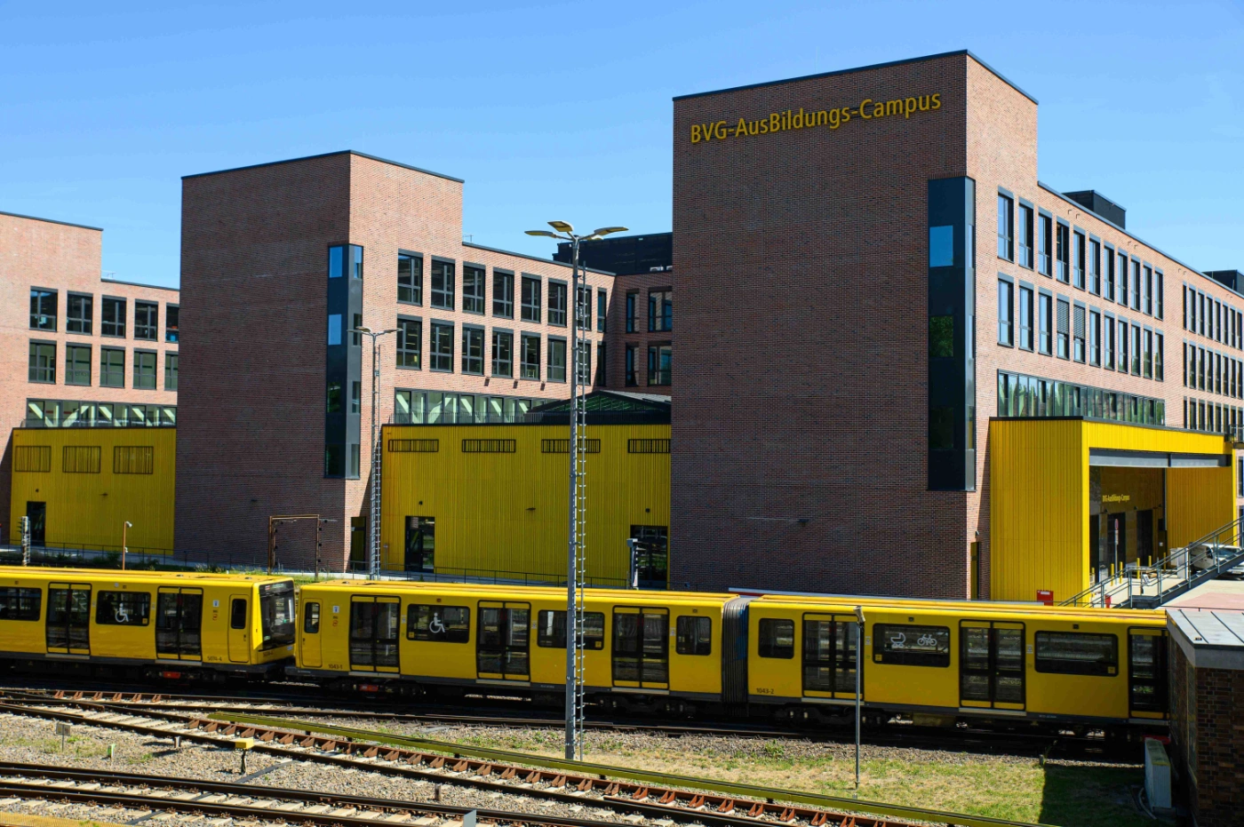 Der BVG-Ausbildungscampus im Manchandelweg bei blauem Himmel mit einer gelben U-Bahn im Vordergrund.