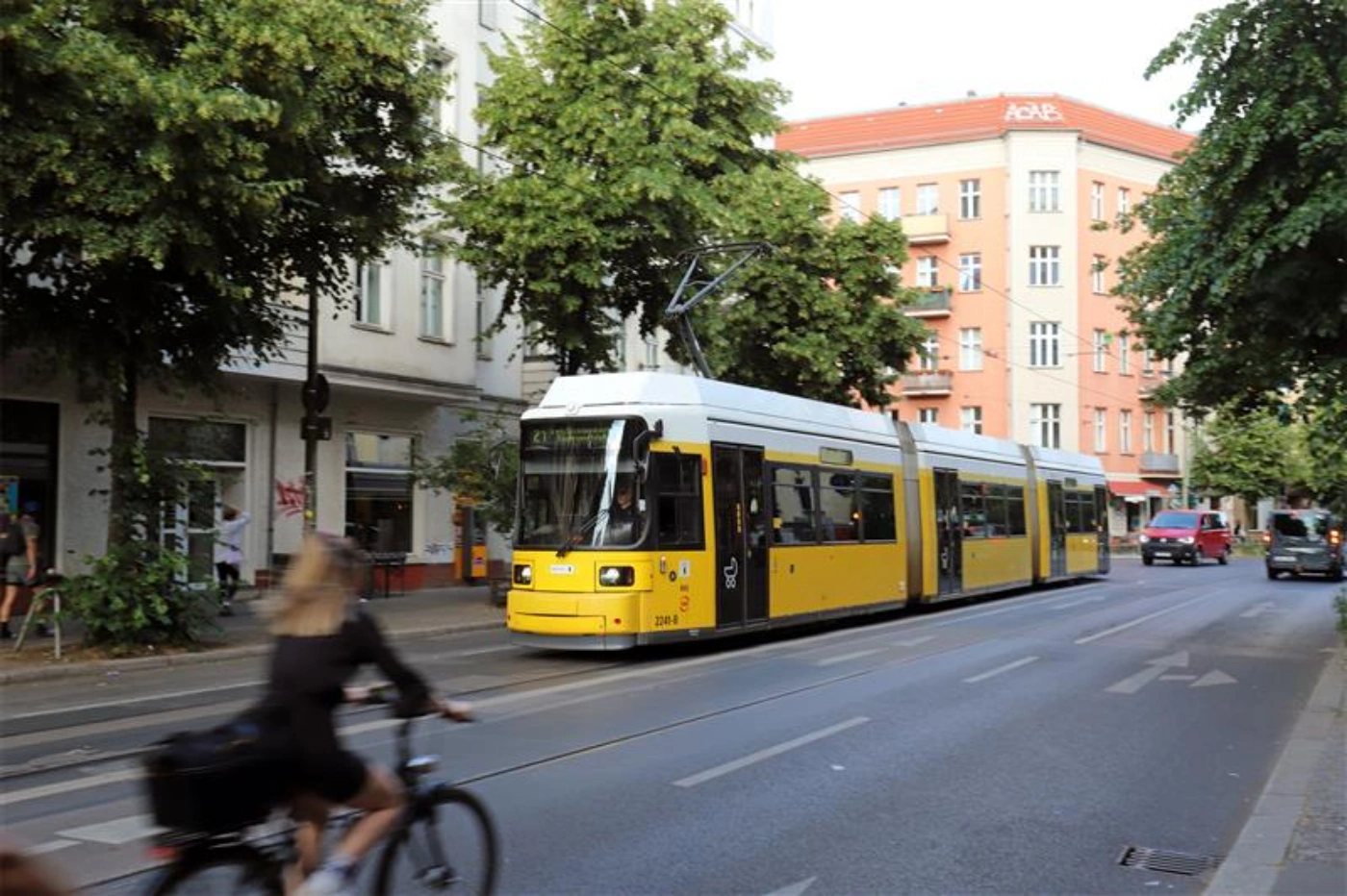 Straßenbahn fährt im Kiez, Frau auf Fahrrad im Vordergrund