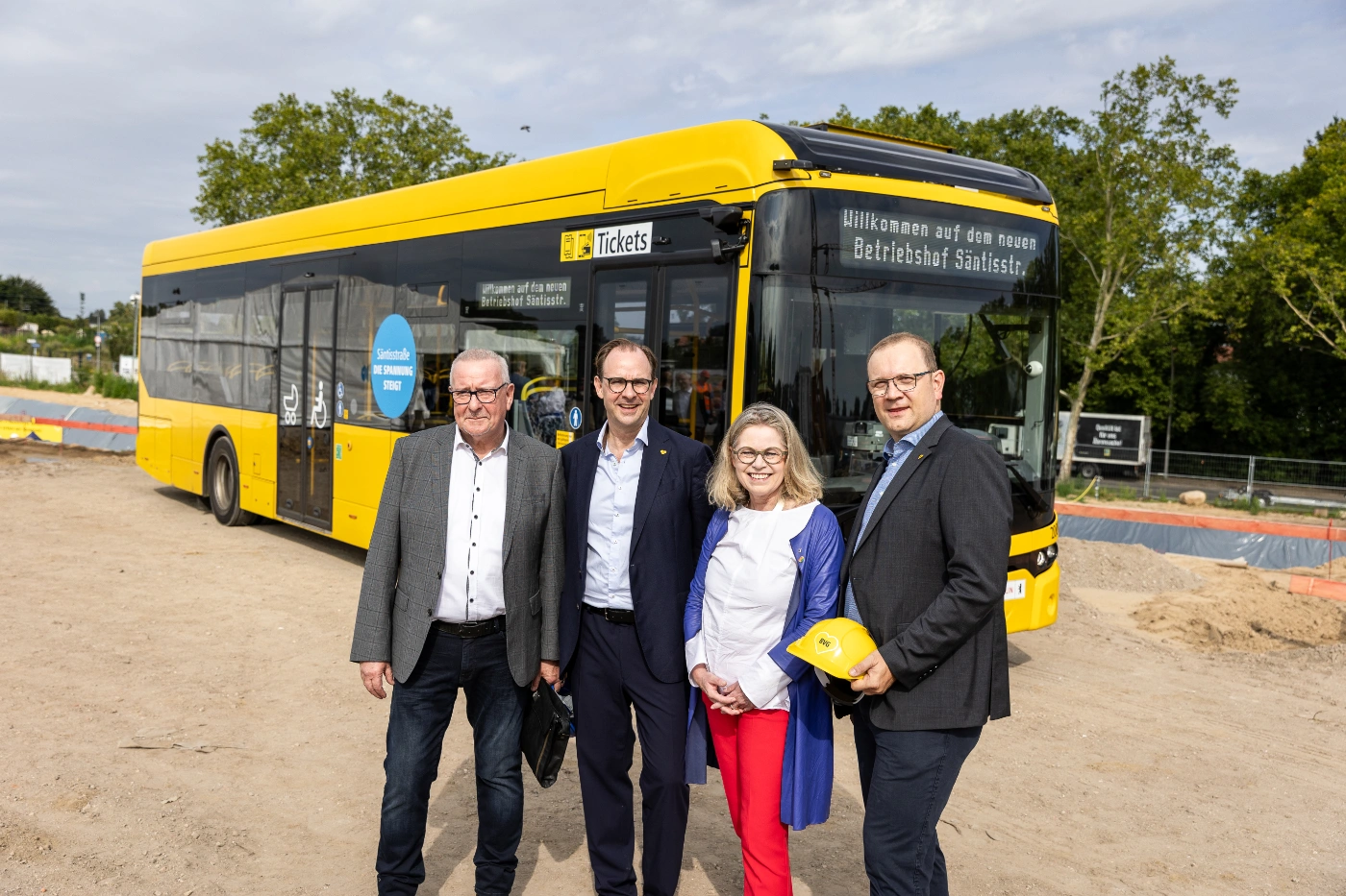 Mehrere Personen stehen vor einem Elektrobus auf einer Baustelle.