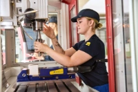 Eine Auszubildende als Industriemechanikerin arbeitet an einer CNC-Drehmaschine und bearbeitet ein Werkstück präzise. Im Hintergrund sind weitere Maschinen und Werkbänke zu sehen.