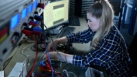 Eine auszubildene Elektronikerin der BVG arbeitet an einem elektrischen Gerät.