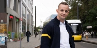 Straßenbahnfahrer Nico steht auf einer Verkehrsinsel in Berlin Mitte - im Hintergrund fährt eine Straßenbahn