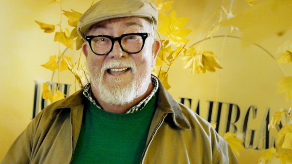 Ronald, Kandidat für IBEF, strahlt in die Kamera: Ein Mann mit beiger Schiebermütze, schwarzer, markanter Brille und weißem Bart.