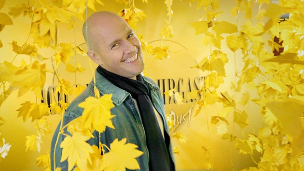 Oli P., Kandidat für IBEF, strählt vor gelbem Hintergrund in die Kamera.