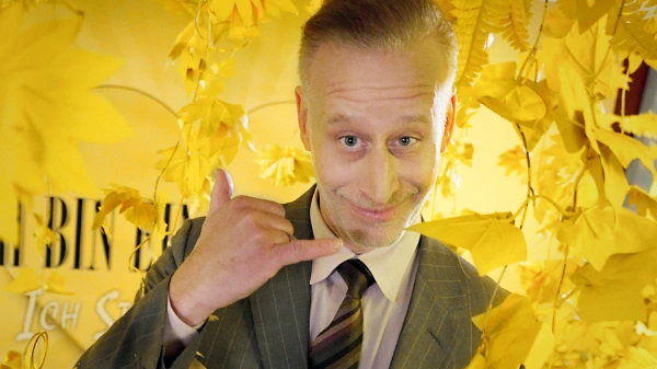 Clemens, Kandidat bei IBEF, schaut verschmitzt in die Kamera: Er trägt Anzug und Krawatte und macht das Zeichen für "Telefonieren""