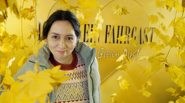 Gisi, Kandidatin bei IBEF, lächelt in die Kamera: Sie hat schwarze Haare, die sie zusammengebunden trägt, und trägt einen Strickpullover mit Winterjacke.